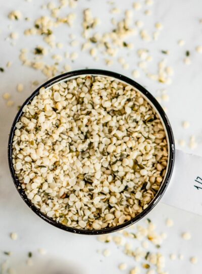 a white measuring cup with a black rim containing hemp hearts spilling over the edges.