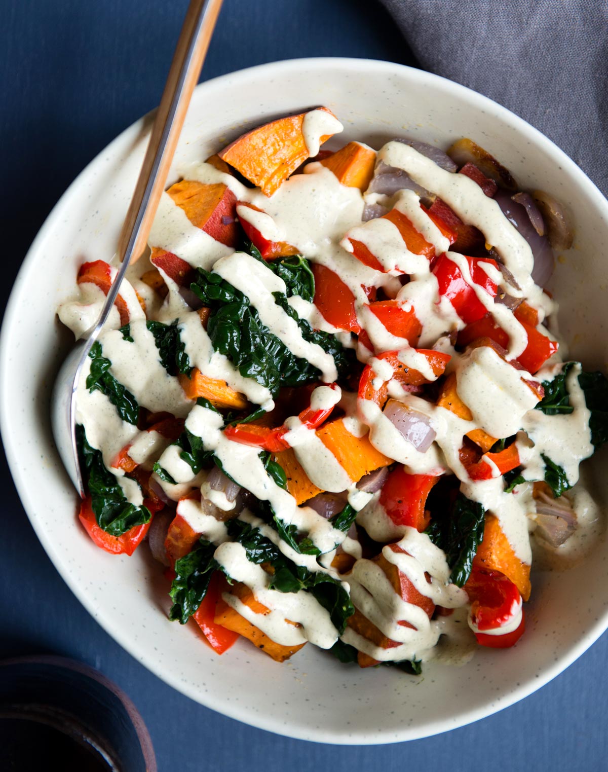 Roasted veggie bowl with sweet potatoes, bell peppers, kale, and a creamy hemp hearts sauce.