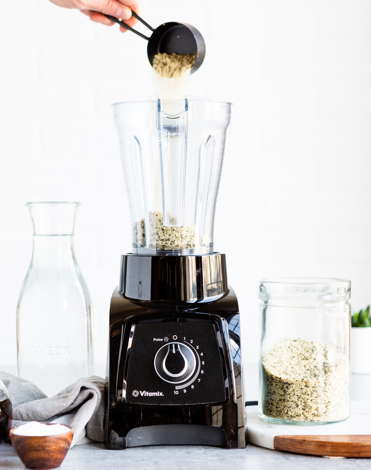 Black blender in a white kitchen with jar of hemp hearts and glass of water.