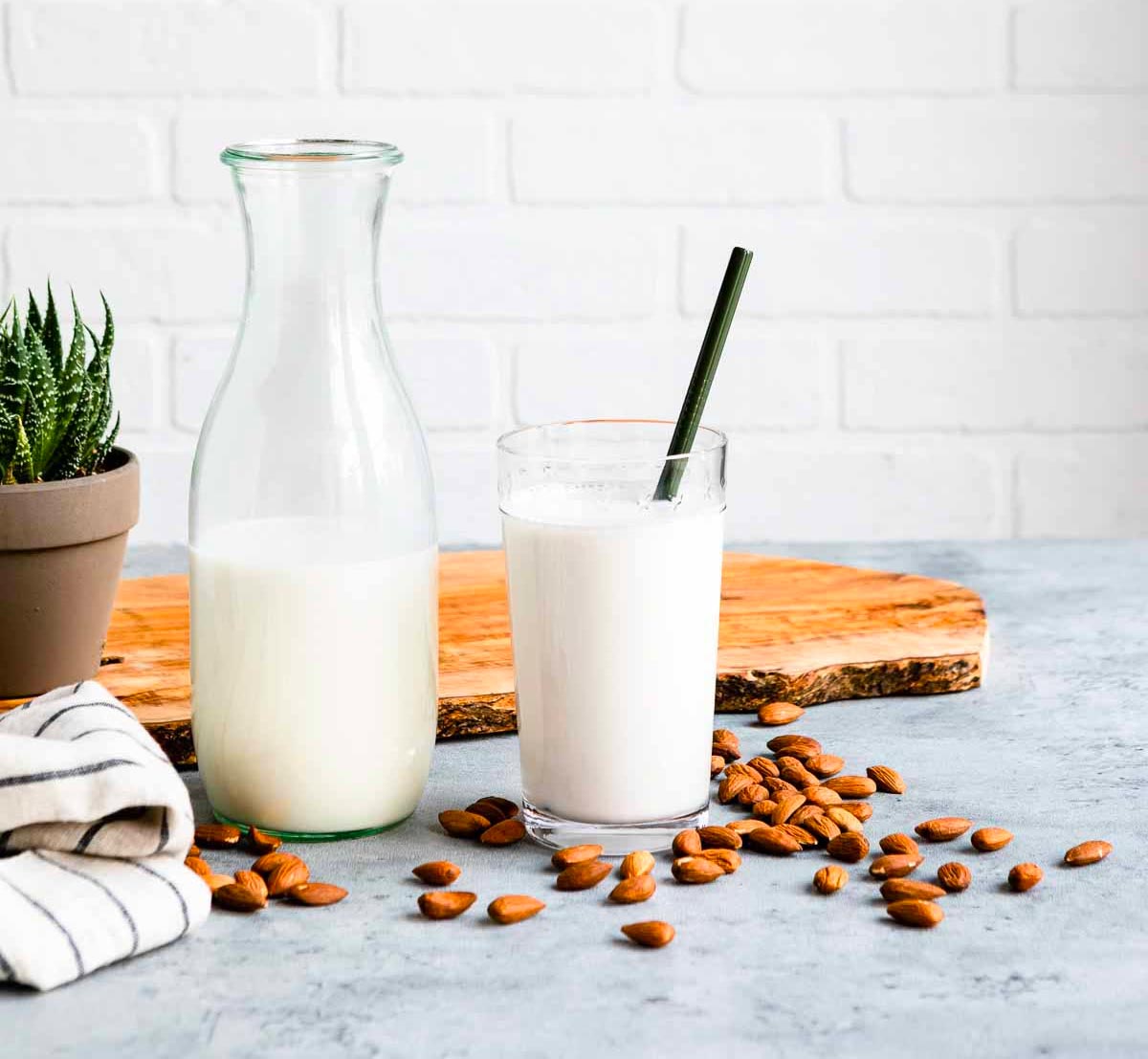 glass jar filled with homemade almond milk next to a glass of almond milk and a green straw.