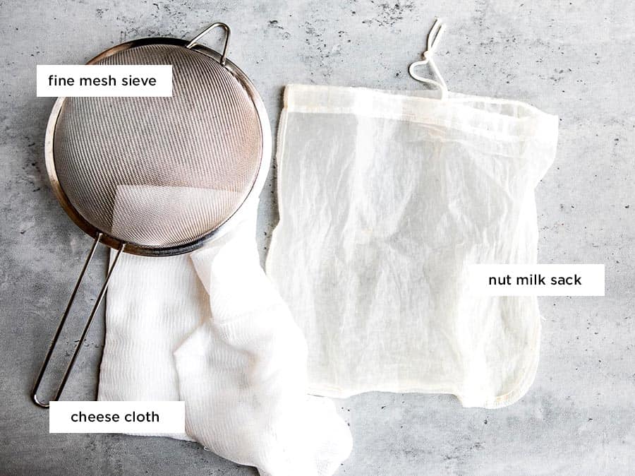 labeled tools for making homemade nut milk including a fine mesh sieve, a nut milk sack and some cheese cloth.