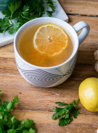 Mug with homemade detox tea recipe with fresh lemon, ginger root and parsley.