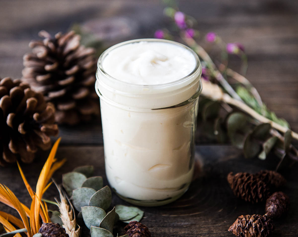 jar of natural deodorant surrounded by pine cones and flowers.