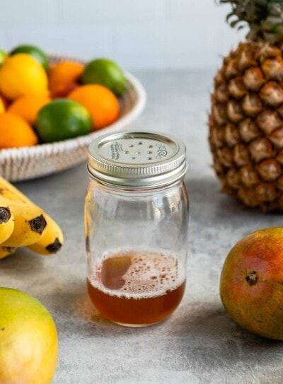 homemade fruit fly trap in glass jar surrounded by fresh fruit.