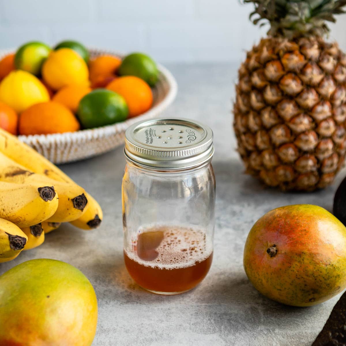 homemade fruit fly trap in glass jar surrounded by fresh fruit.