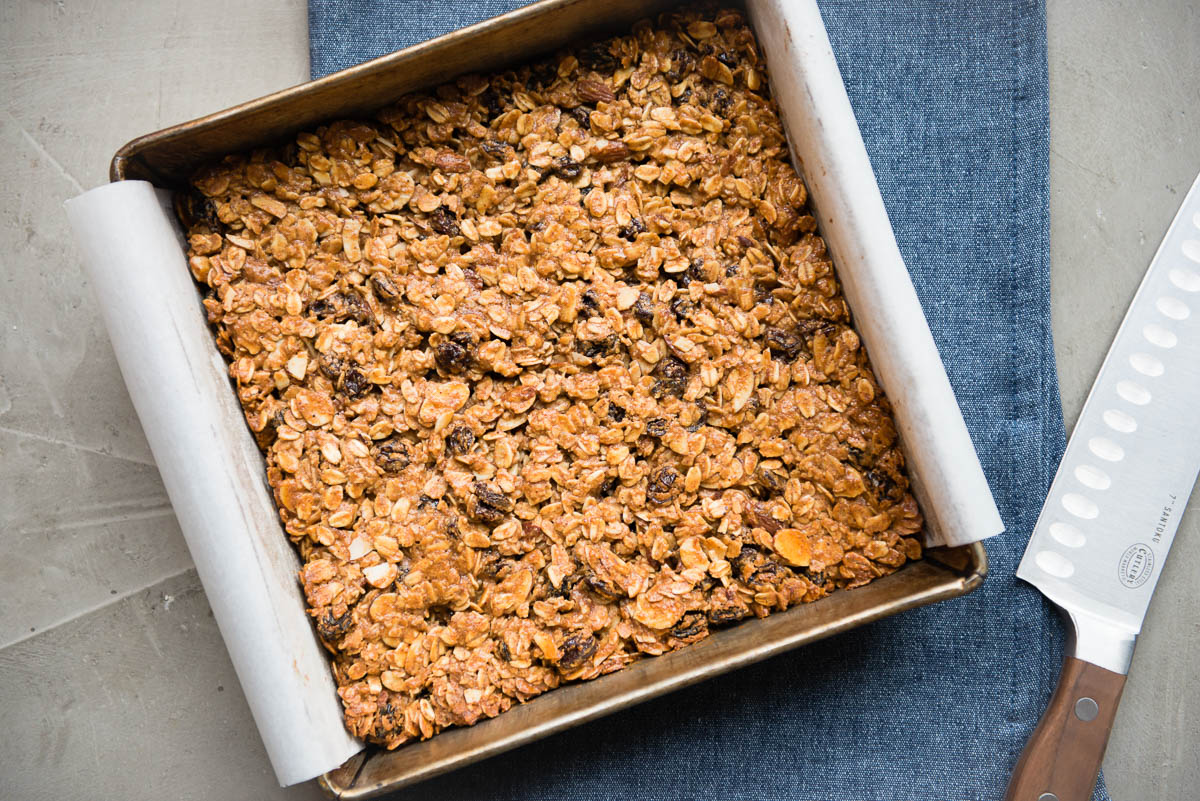 chewy granola bar recipe in a baking dish lined with parchment paper, ready to be cut into squares.