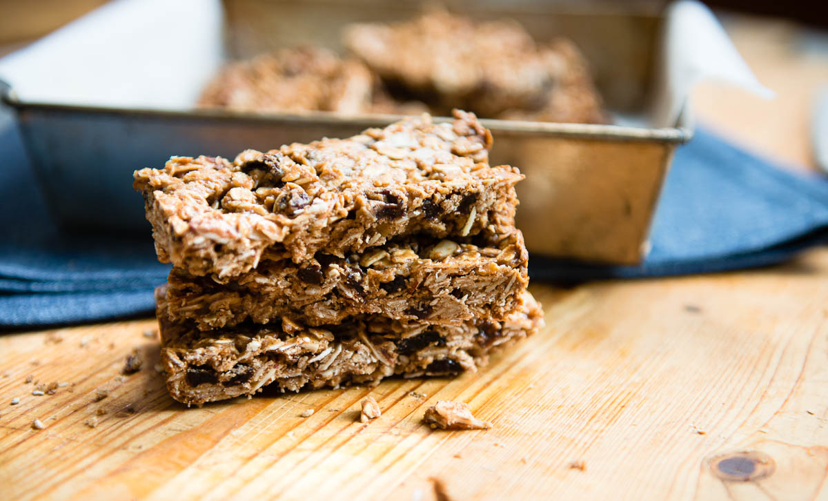 homemade granola bars in a stack next to a baking pan on a wooden table.