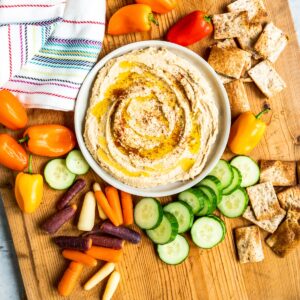 Bowl of homemade hummus surrounded by vegetables.