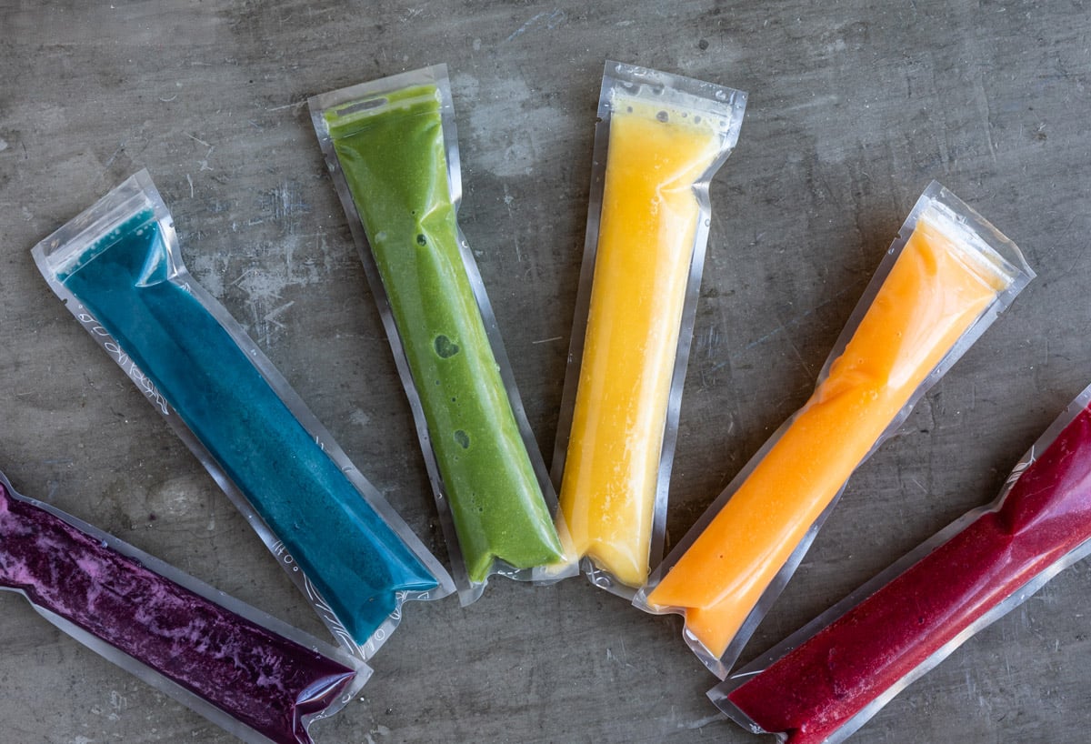 Variety of frozen homemade ice pops on counter in popsicle sleeves.