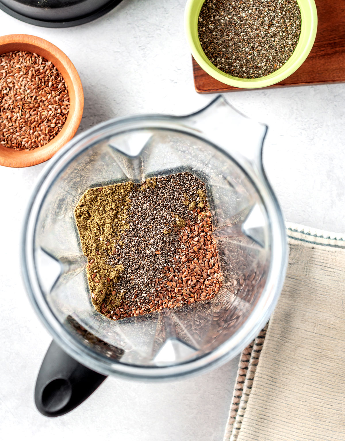 Overhead view of flax, chia, and hemp seeds in a blender, preparing to make homemade protein powder recipe.