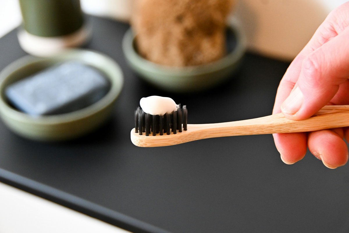 A hand holding a wooden toothbrush with a glob of homemade toothpaste on the bristles.