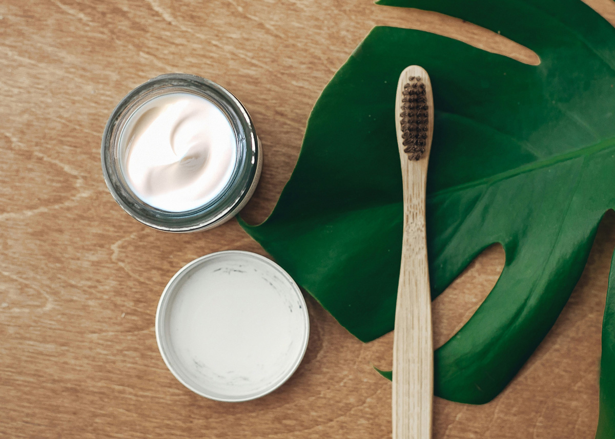 A wooden toothbrush on a counter next to a jar of toothpaste.
