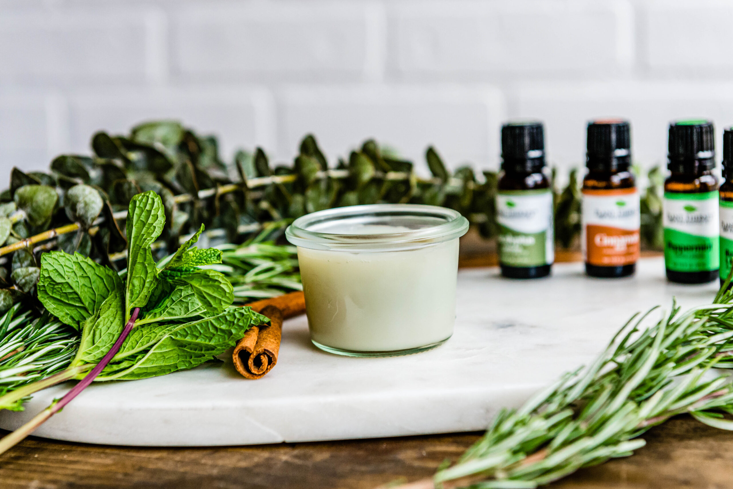 glass jar of natural decongestant on marble tray surrounded by fresh herbs and spices.