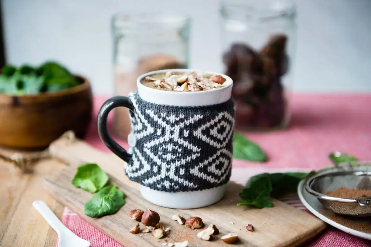hot chocolate smoothie topped with hazelnuts and whipped cream in a mug with a knit wrap.