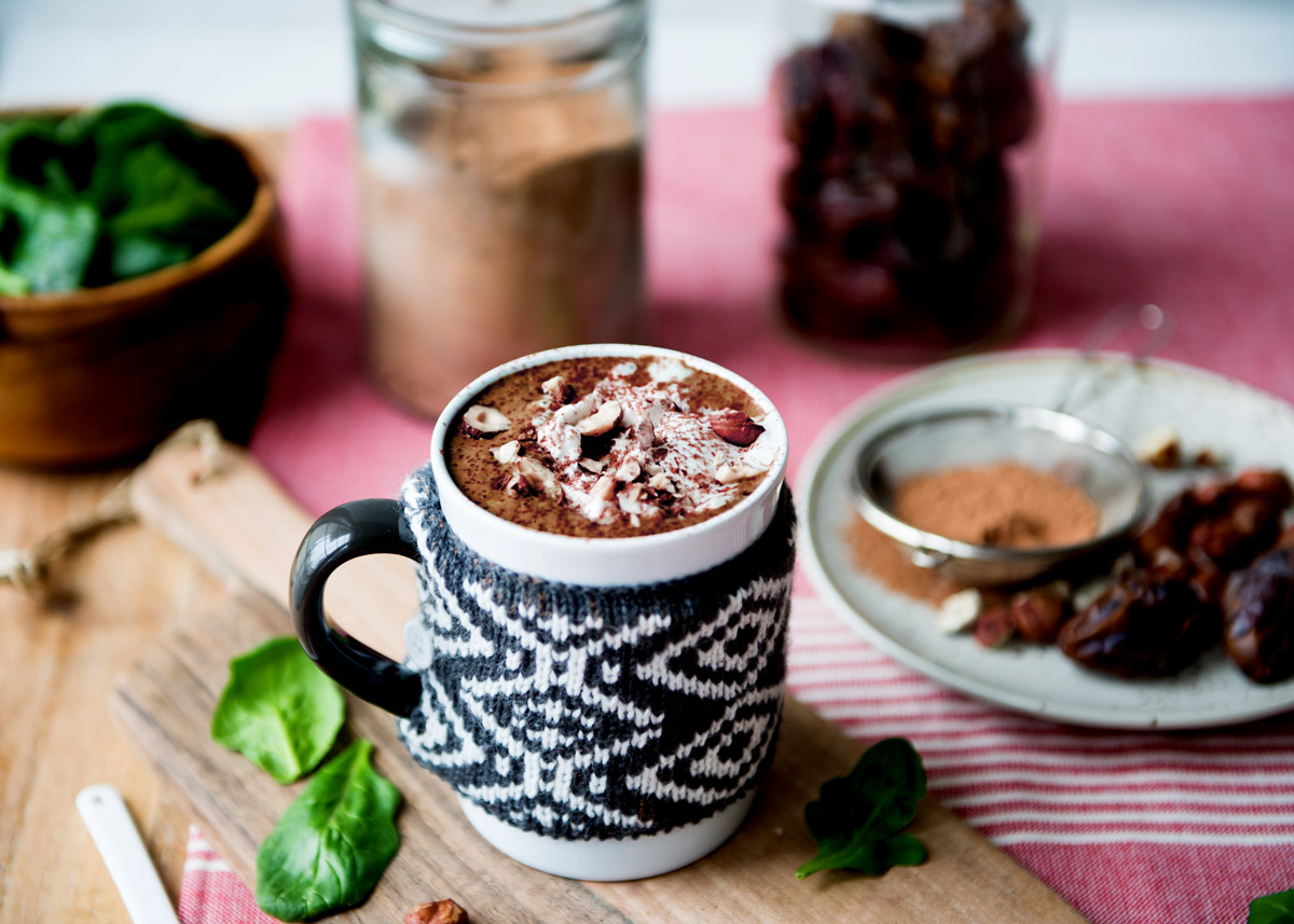 hot chocolate smoothie topped with hazelnuts and whipped cream in a mug with a knit wrap.