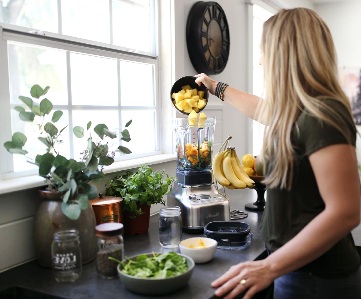 Jen Hansard in her kitchen making a smoothie and putting chopped fruits in a blender.