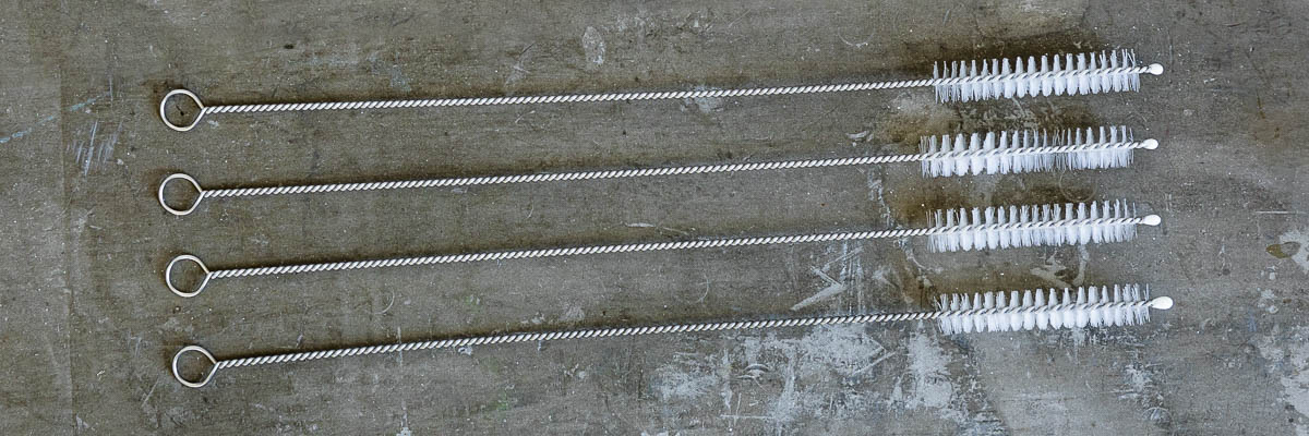 4 wire straw cleaners with white bristles on a concrete countertop. 