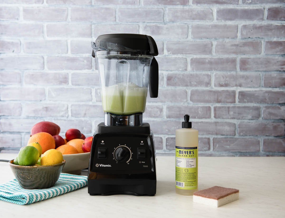 vitamix blender with soap suds inside next to a bottle of dish soap, showing how to clean a blender.