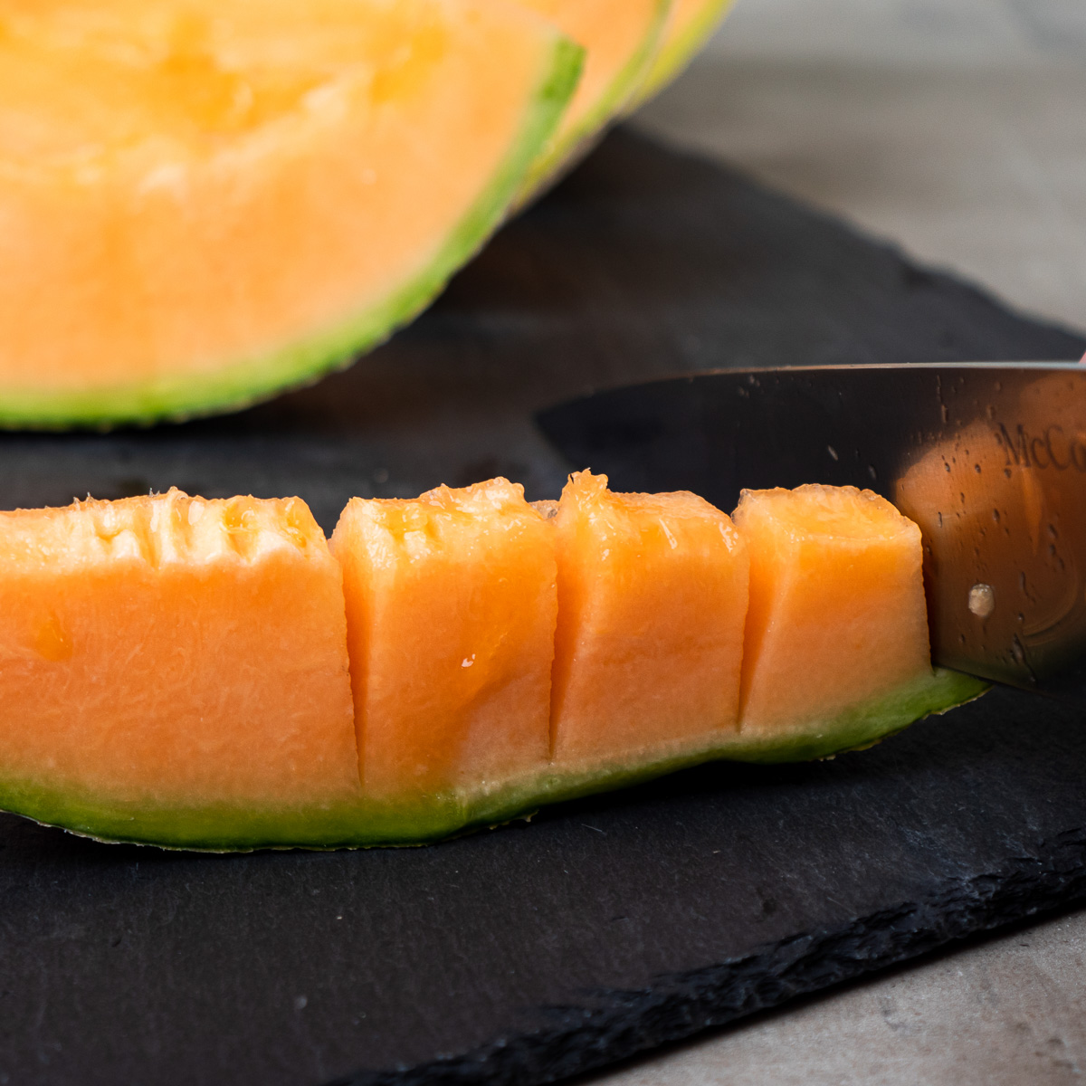 A section of cantaloupe being sliced into chunks while still attached to the rind.
