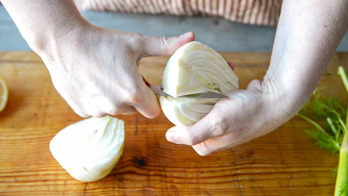 2 hands cutting a fennel bulb into sections using a paring knife.