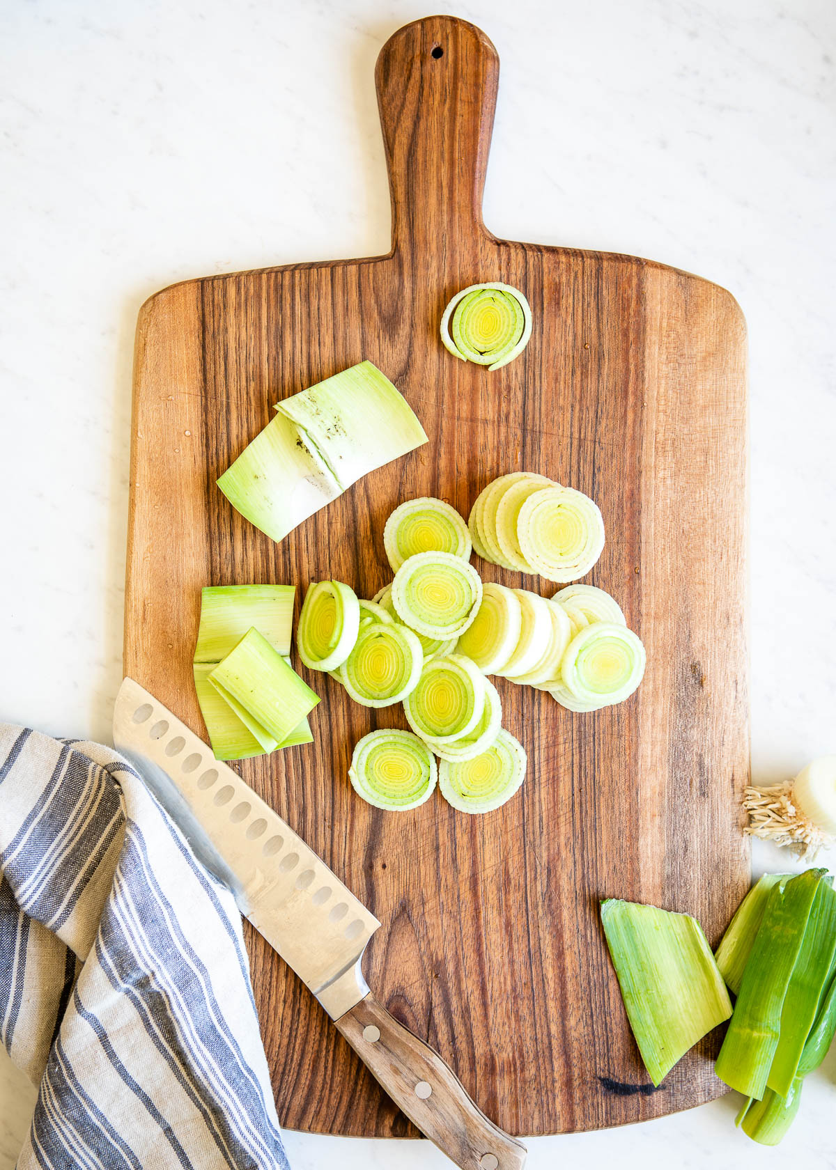 several thin slices of leek on a wooden cutting board.