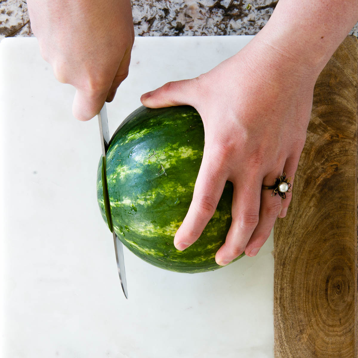 hand holding a small watermelon and slicing with a chef's knife.