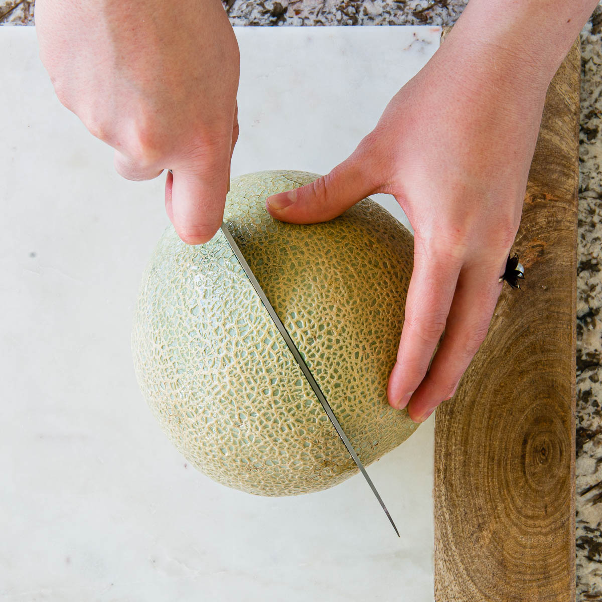 slicing a whole cantaloupe in half with a chef's knife.