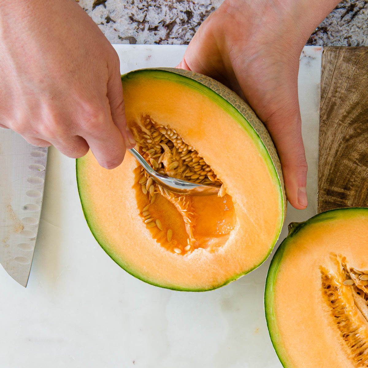 scooping out the seeds from halves of a cantaloupe to show how to cut a cantaloupe.