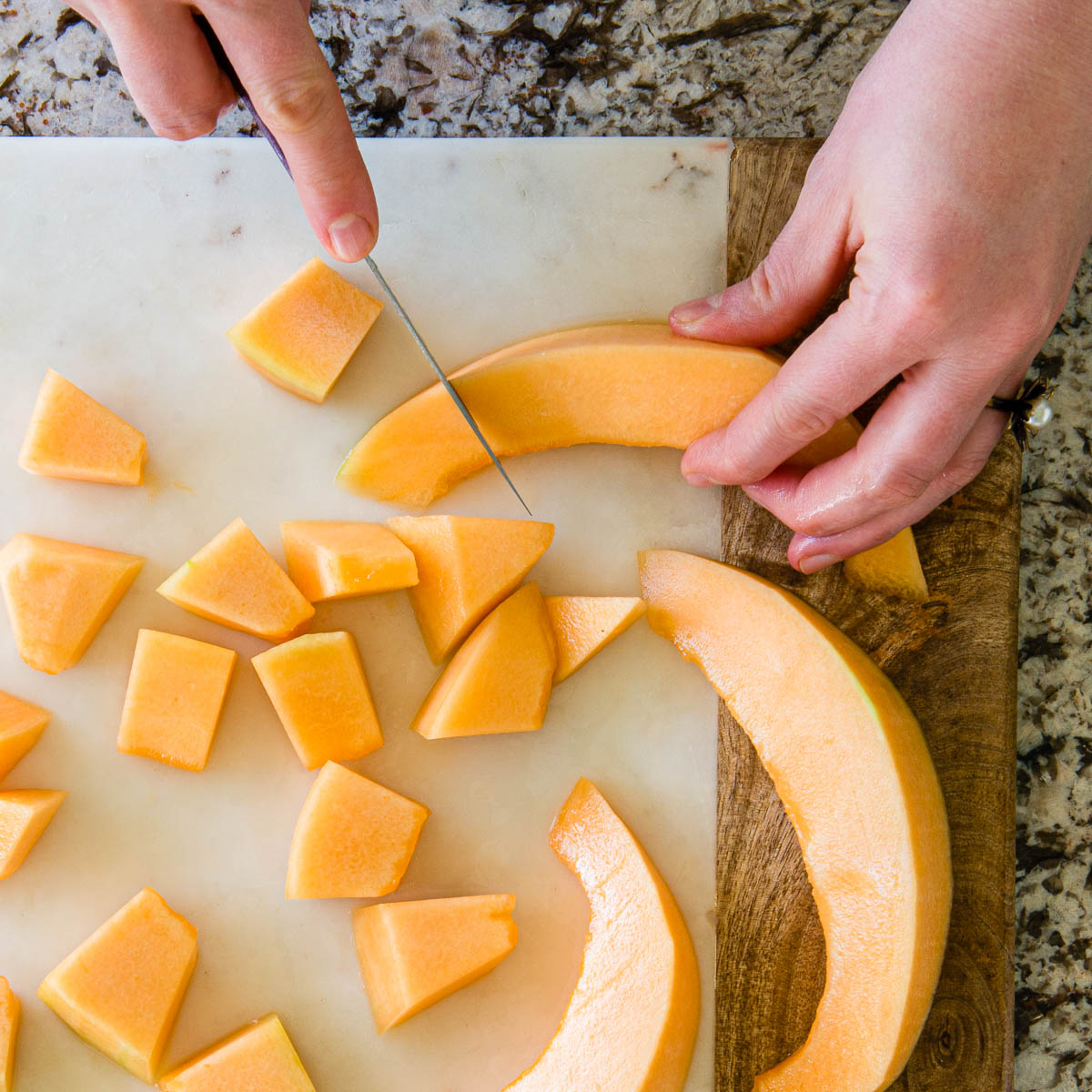 slicing small pieces of cantaloupe from large wedges on a marble cutting board.