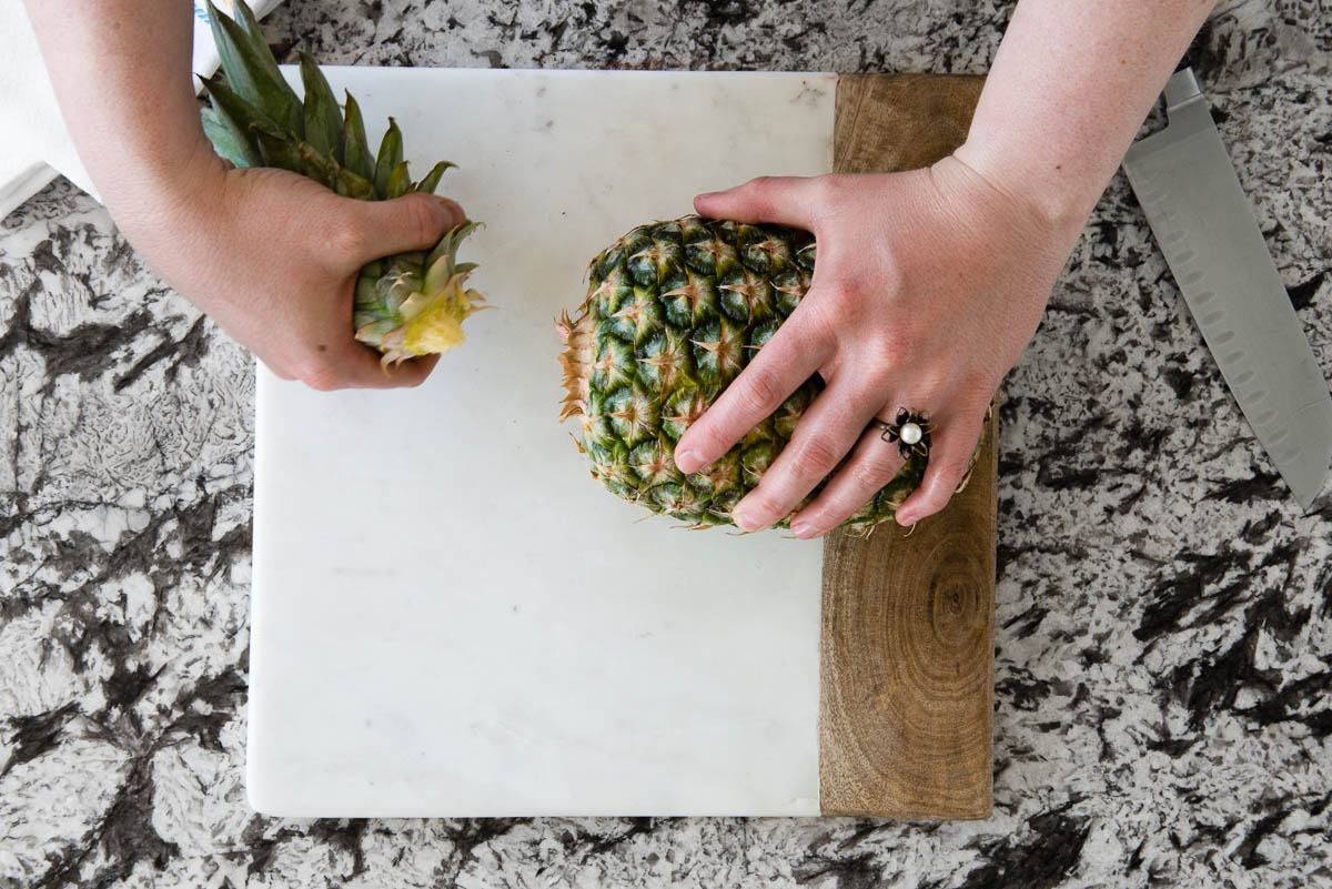 showing how to remove the pineapple stem on a marble cutting board.