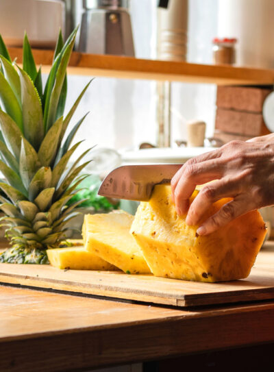 cutting pineapple with a knife on a cutting board.