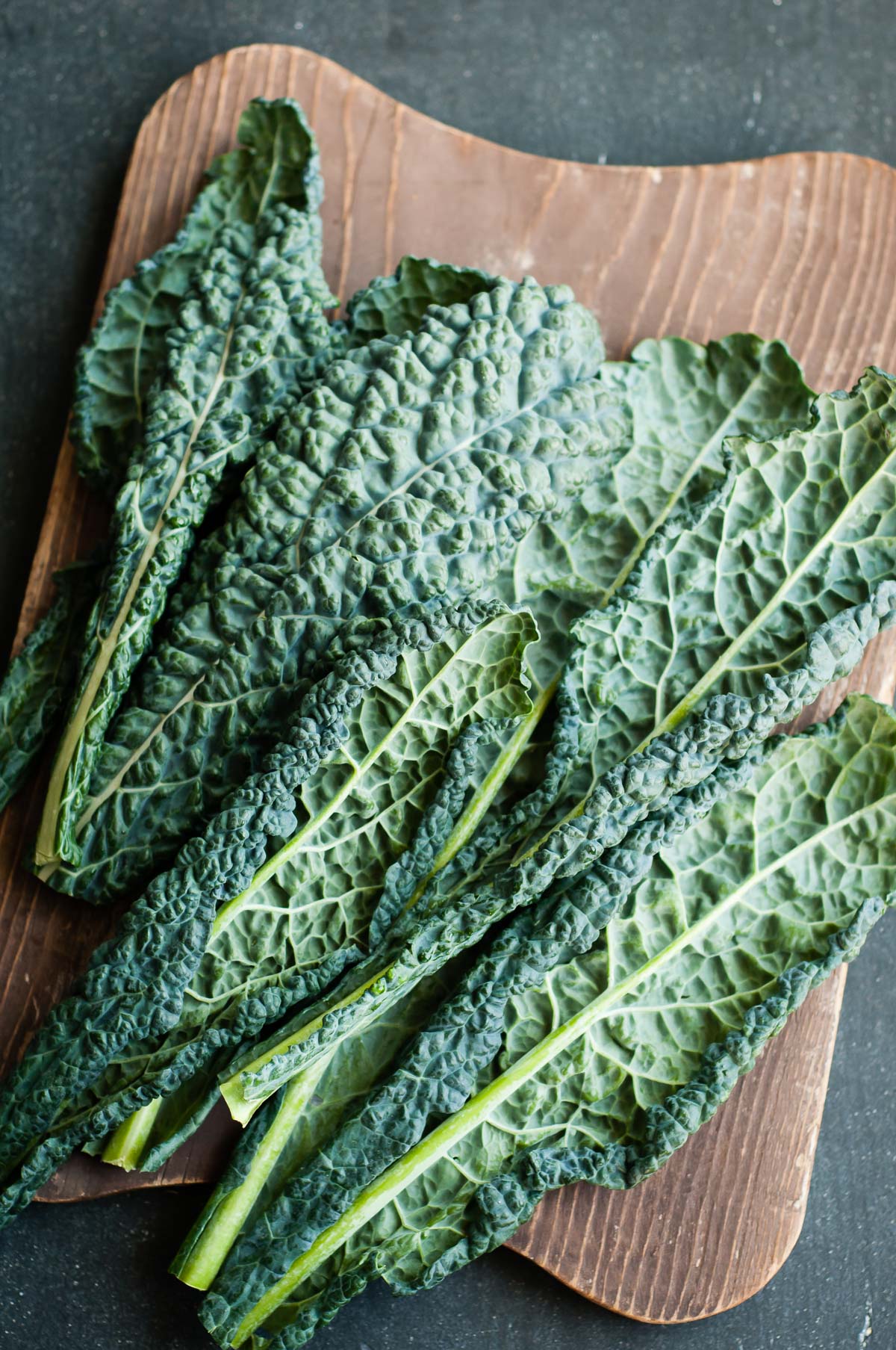 Fresh kale with stems intact laid out on a cutting board