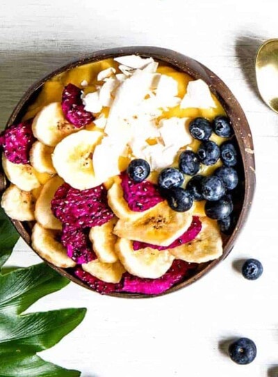 smoothie bowl recipe in a coconut bowl topped with dried dragon fruit, bananas, blueberries and coconut.