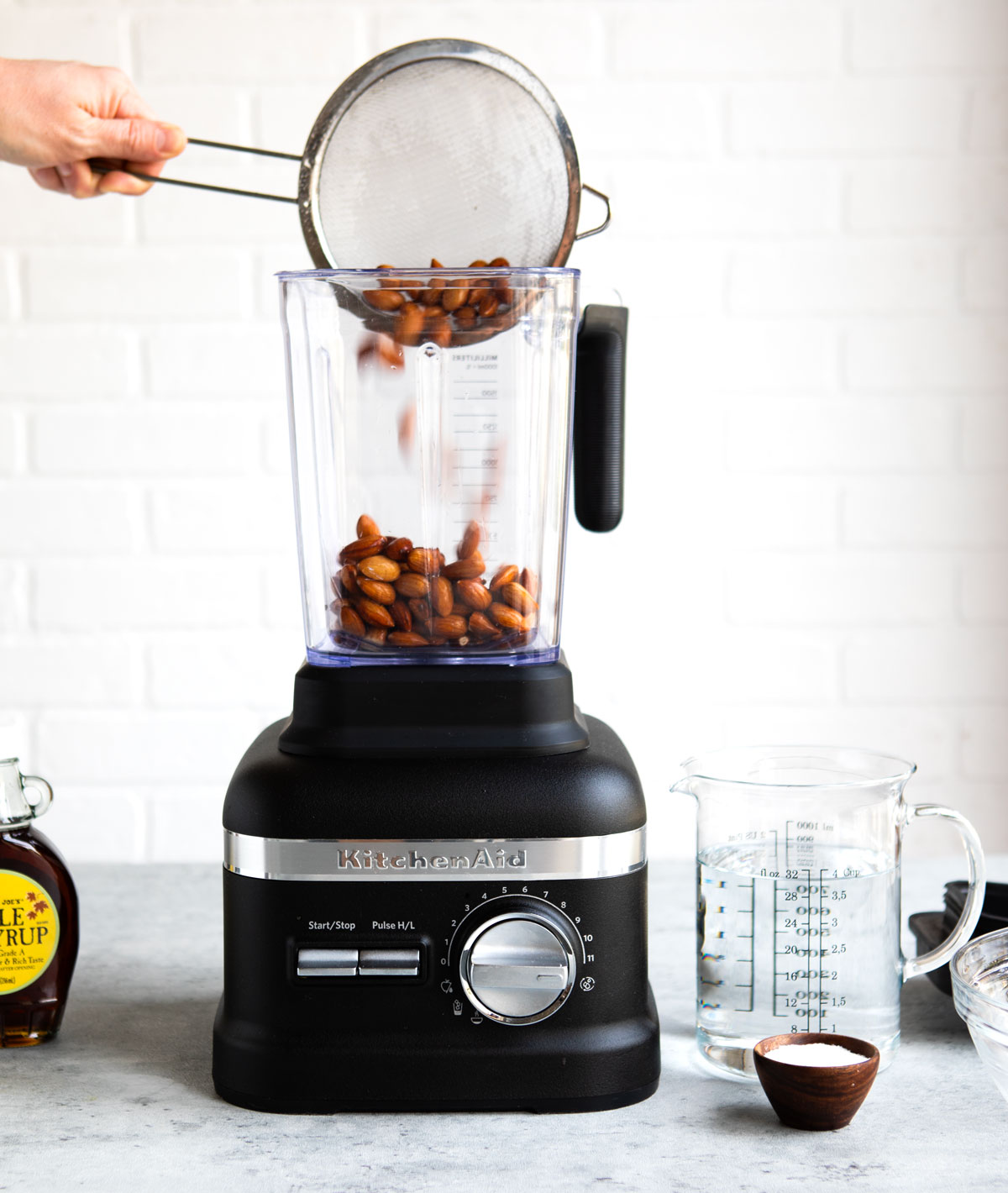 A person pouring almonds into a blender to make homemade almond milk.