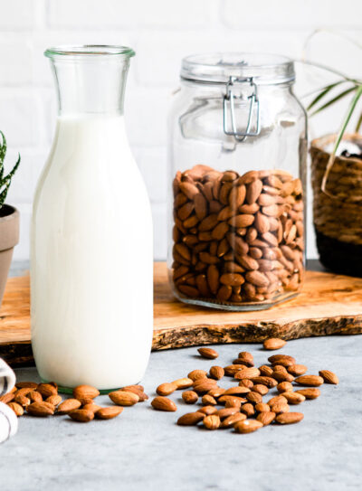 Almond milk in a glass carafe with jar of almonds in background.