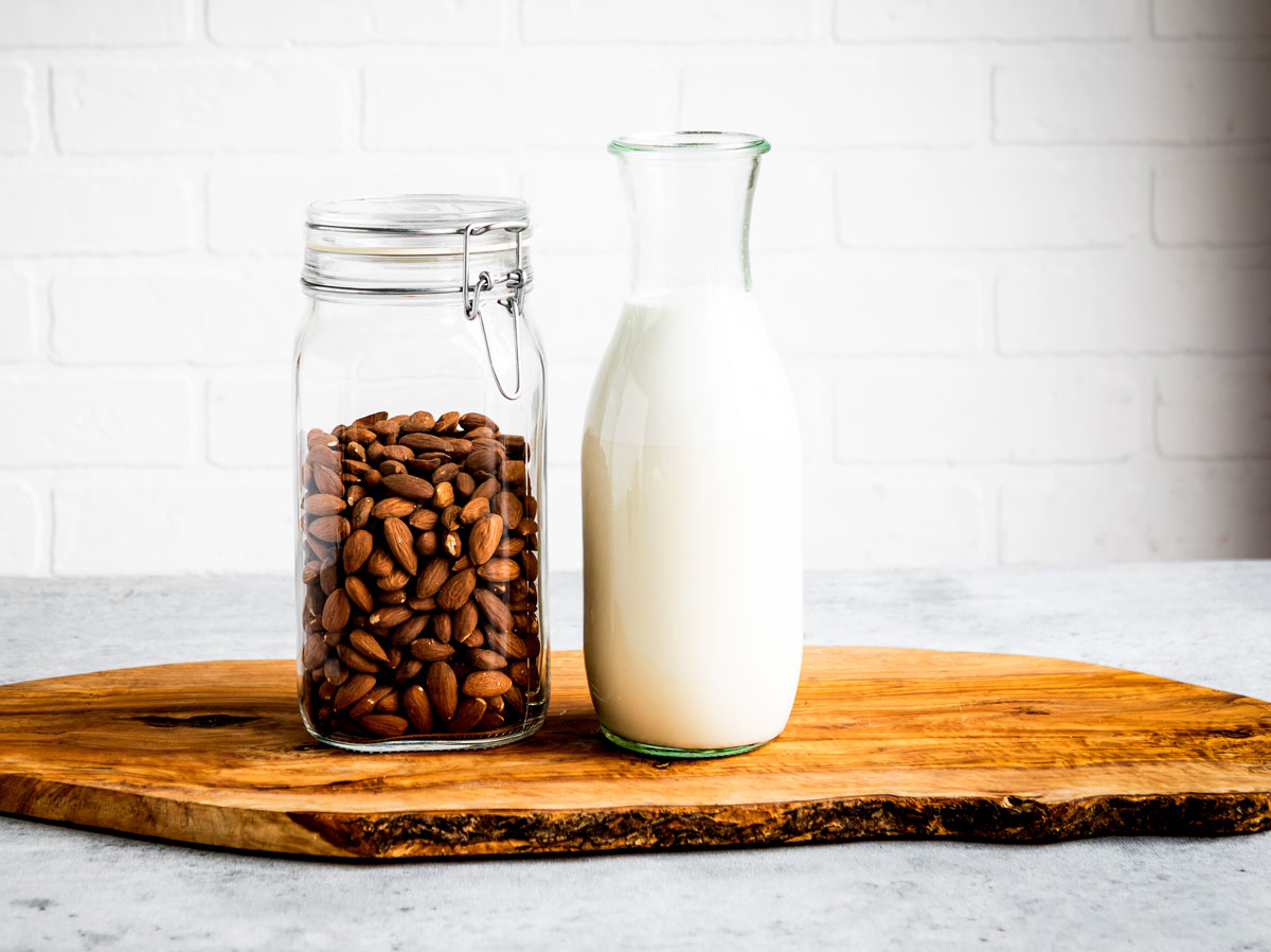 A jar of almonds and a bottle of almond milk on a wooden board.