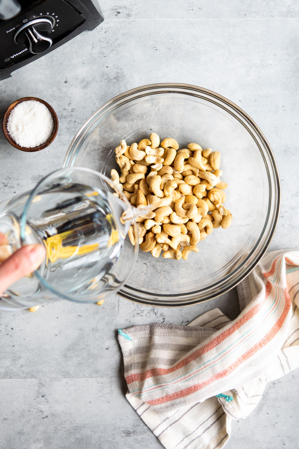 Pouring water from a measuring cup into a bowl of cashews.