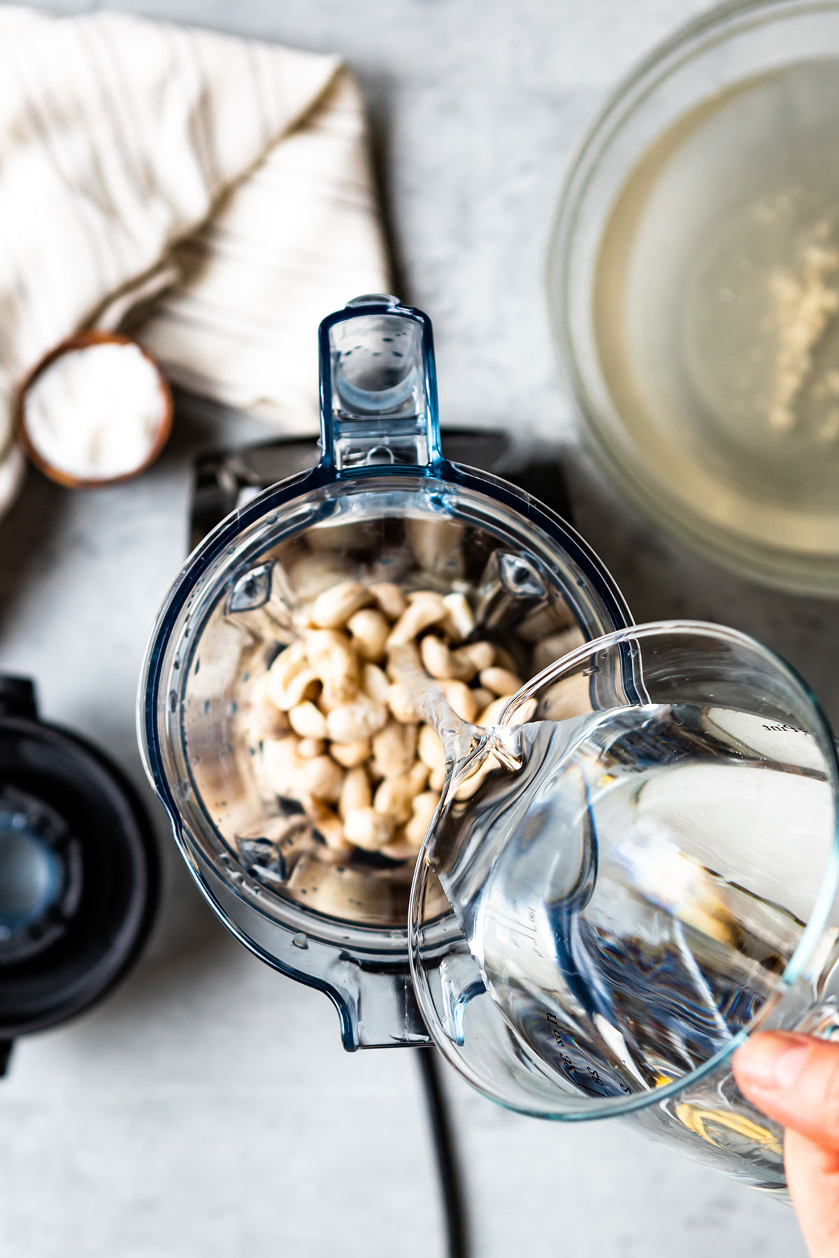 Pouring water into a blender with cashews.