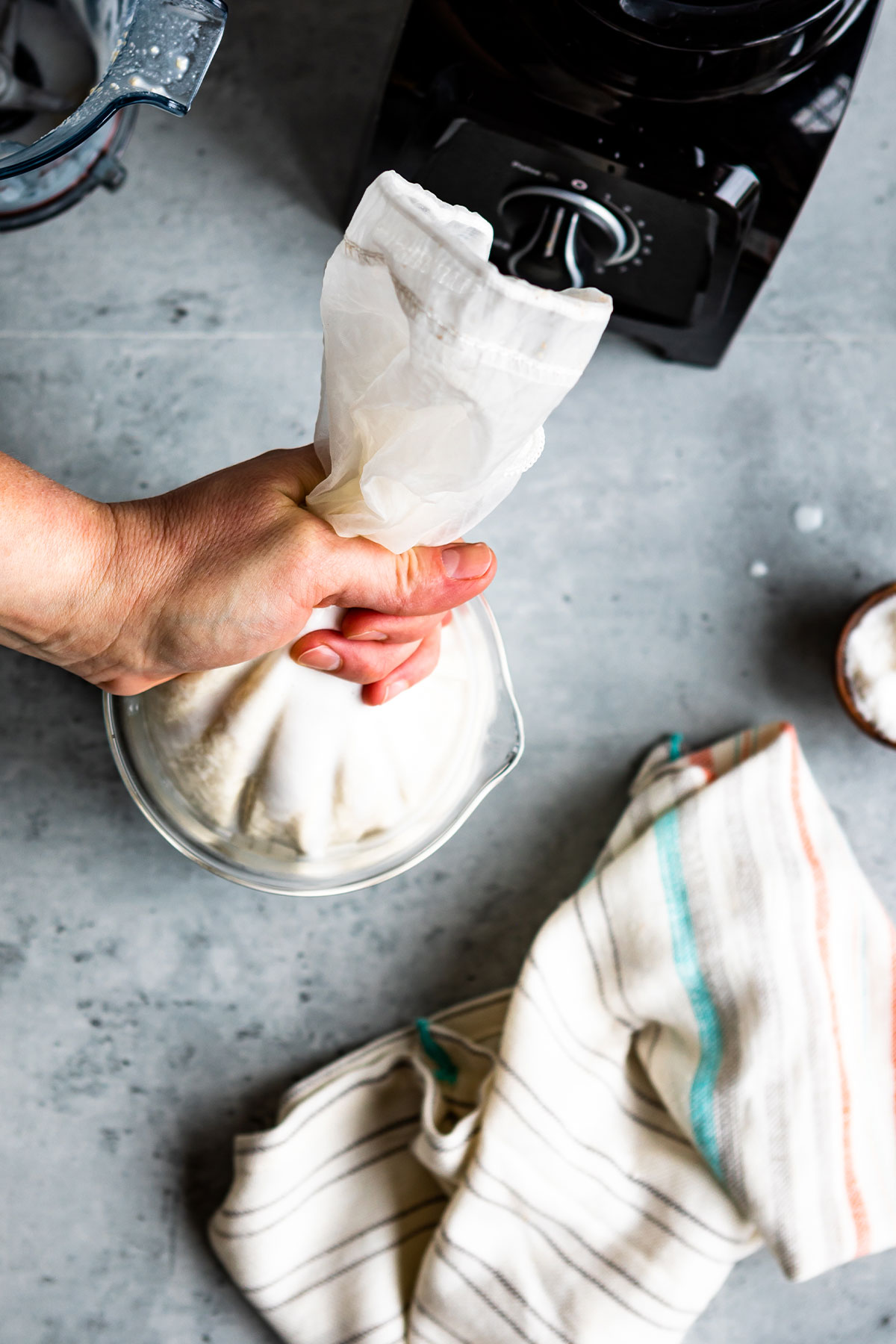 Squeezing cashews in nut milk bag into a glass bowl.