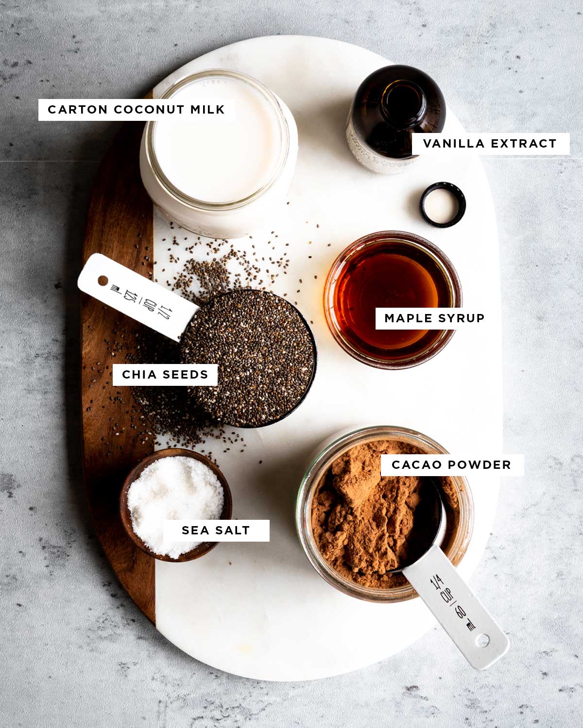 ingredients for how to make chia pudding including carton coconut milk, vanilla extract, maple syrup, chia seeds, sea salt and cacao powder.
