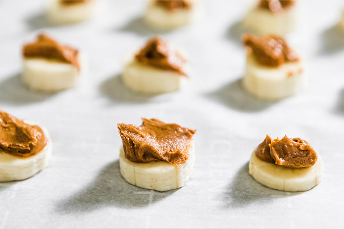 putting sliced bananas on baking sheet with almond butter on top.
