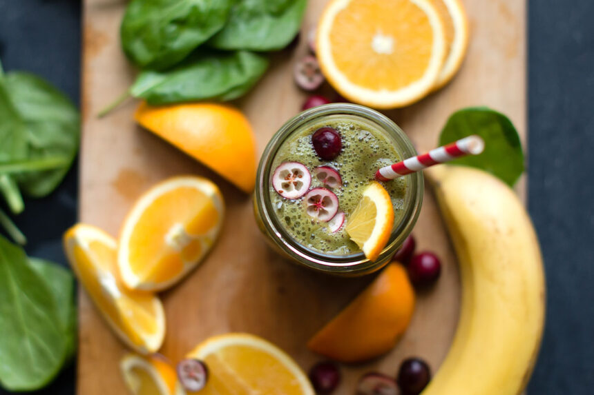 glass of green smoothie with sliced cranberries on top.