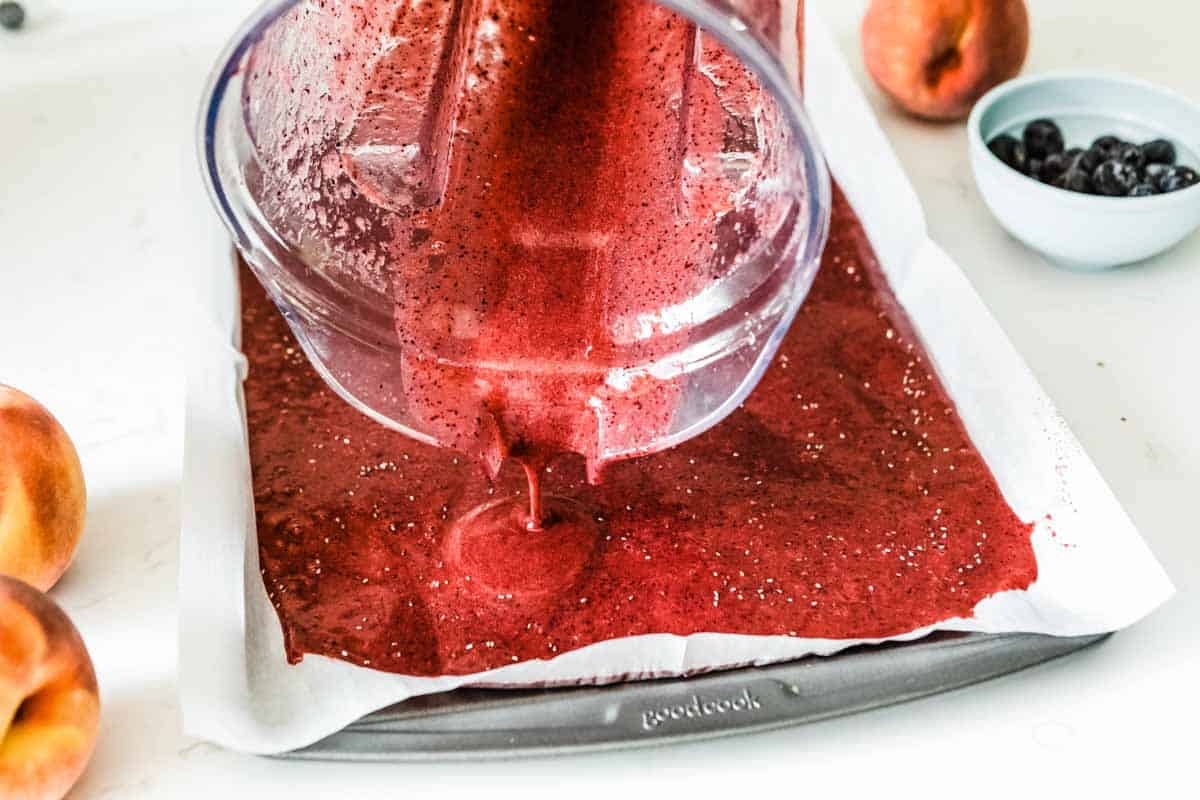 pouring pureed fruit onto a parchment lined baking tray for homemade fruit leather.