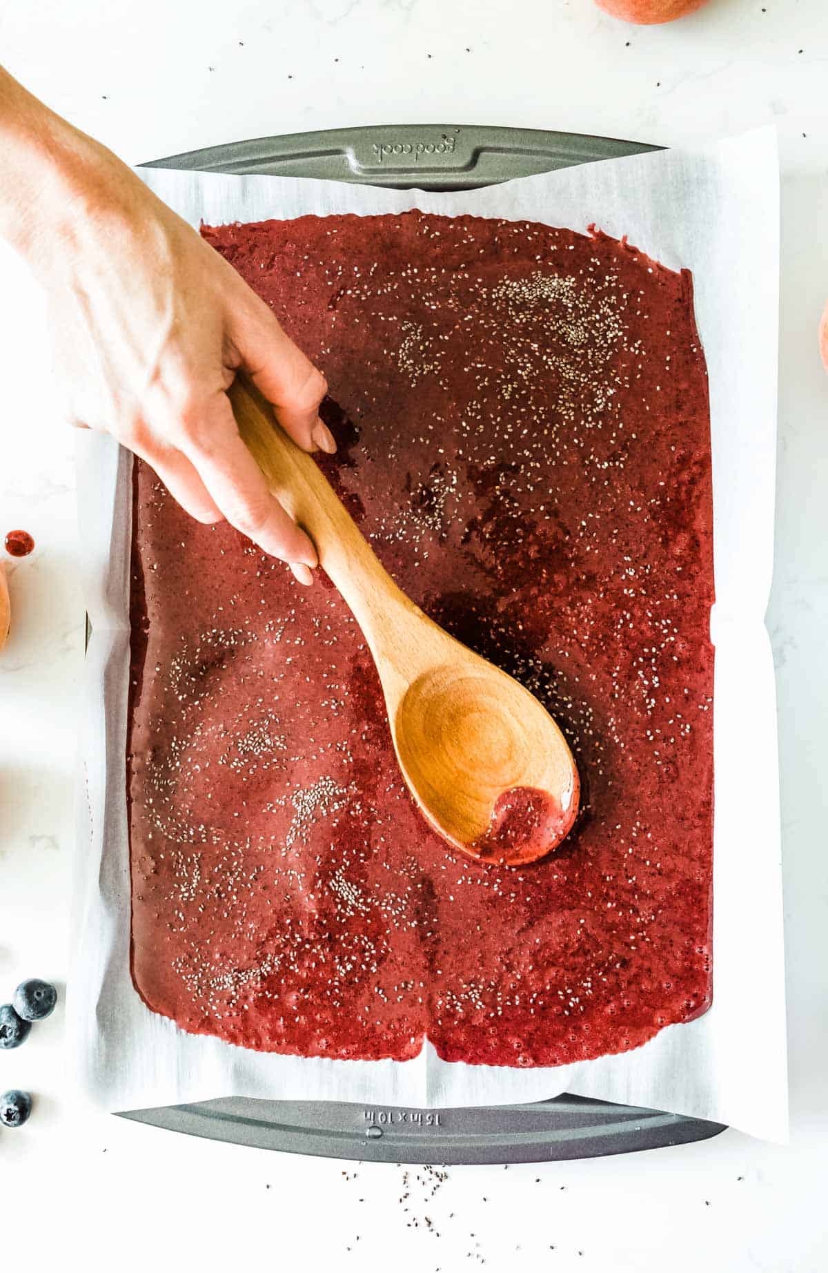 spreading out pureed fruit in a parchment-lined baking tray with chia seeds sprinkled over top.