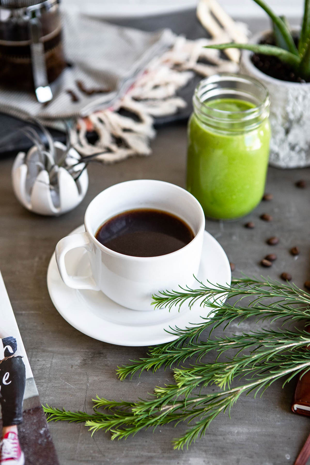 healthy coffee in a white cup on a white plate next to a jar of green smoothie.
