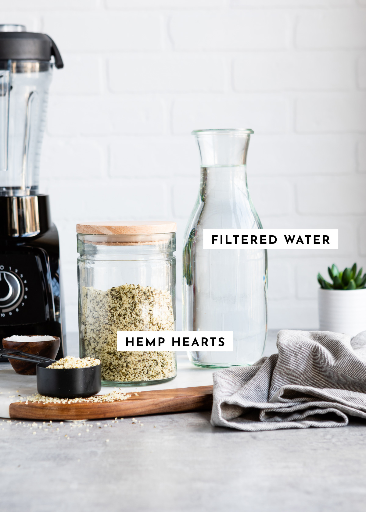 Hemp hearts and water on a counter with a blender in the background to make hemp milk.