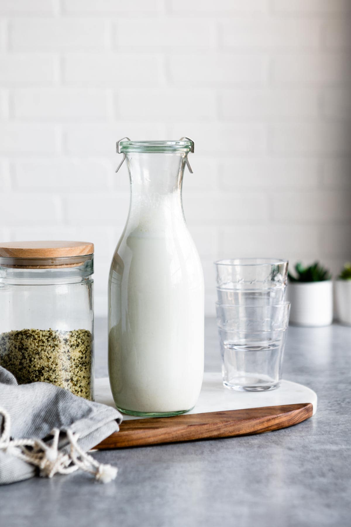 glass jar of hemp milk next to a jar of hemp hearts and short glasses.