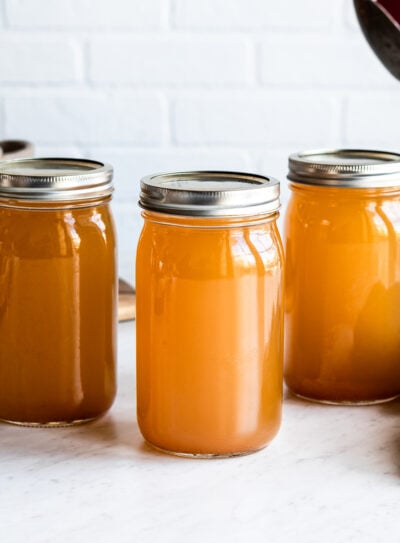 Three mason jars with homemade vegetable stock on white kitchen counter
