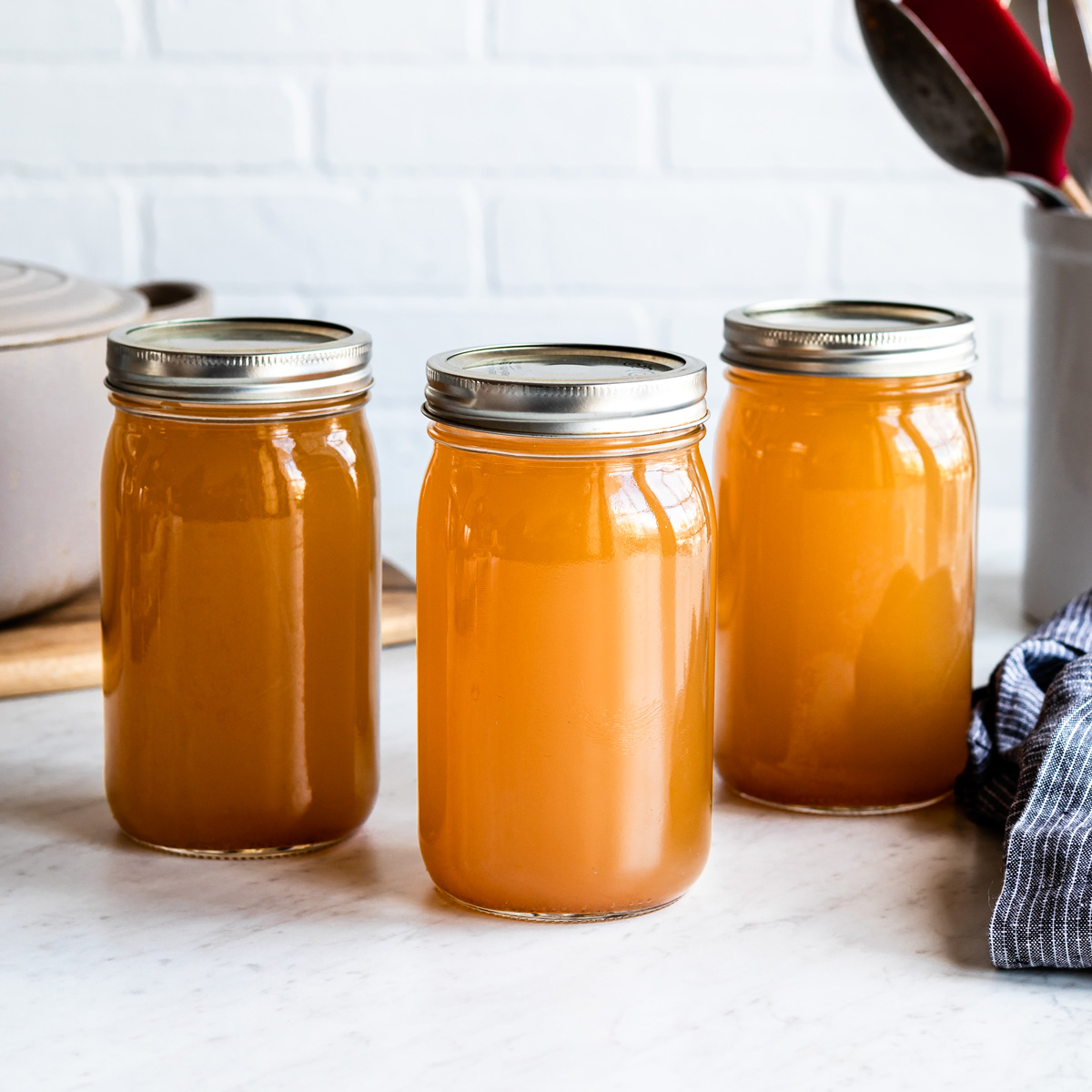 Three mason jars with homemade vegetable stock on white kitchen counter