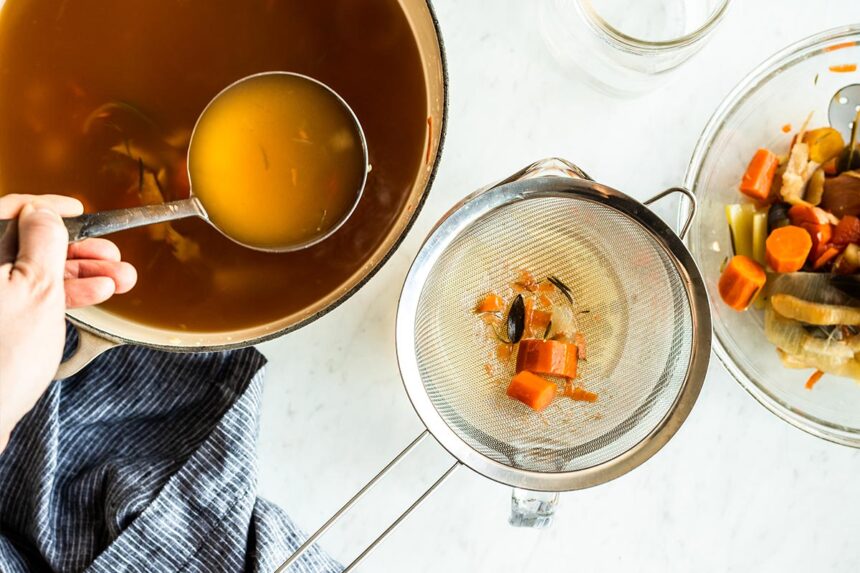 Scooping vegetable broth into a sieve to separate the vegetables from the liquid.